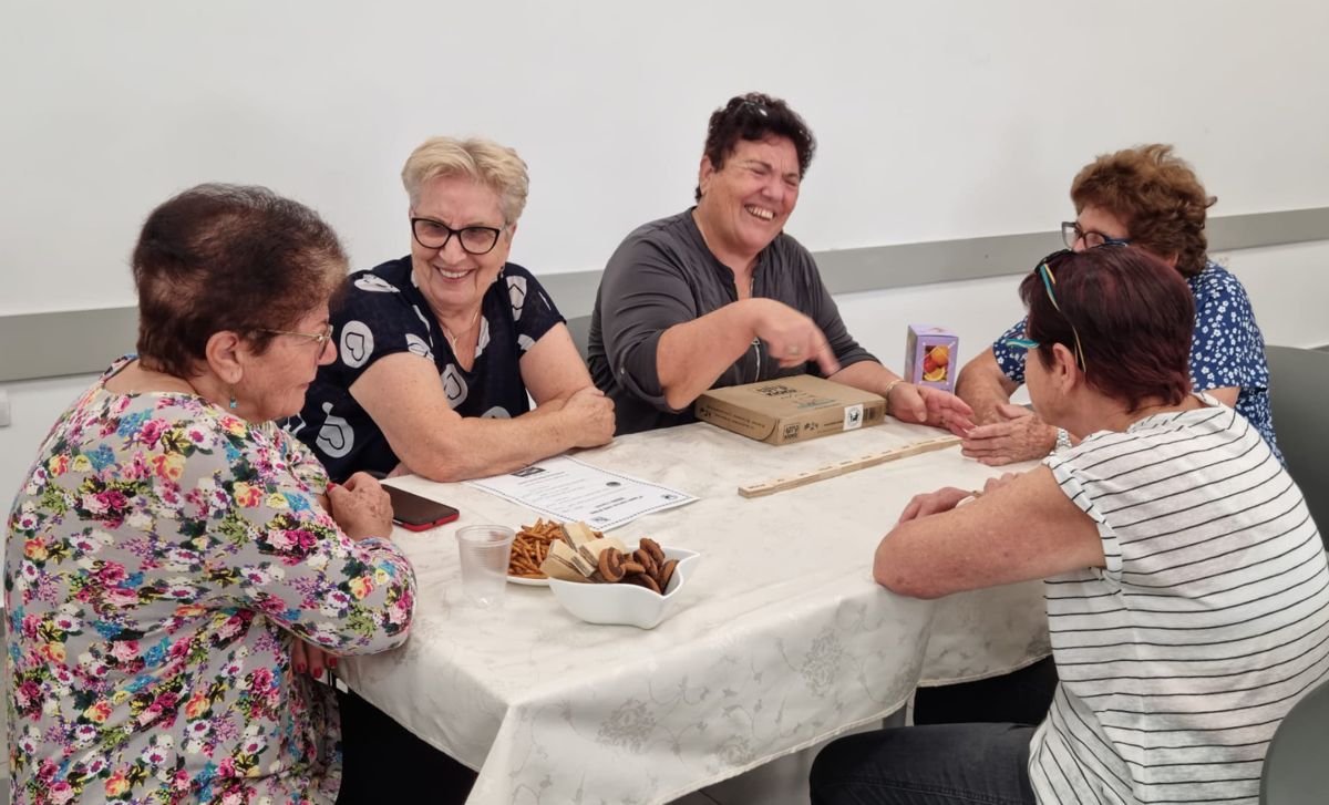 קבוצת נשים משחקת קיוקו סביב שולחן עם ערכת המשחק